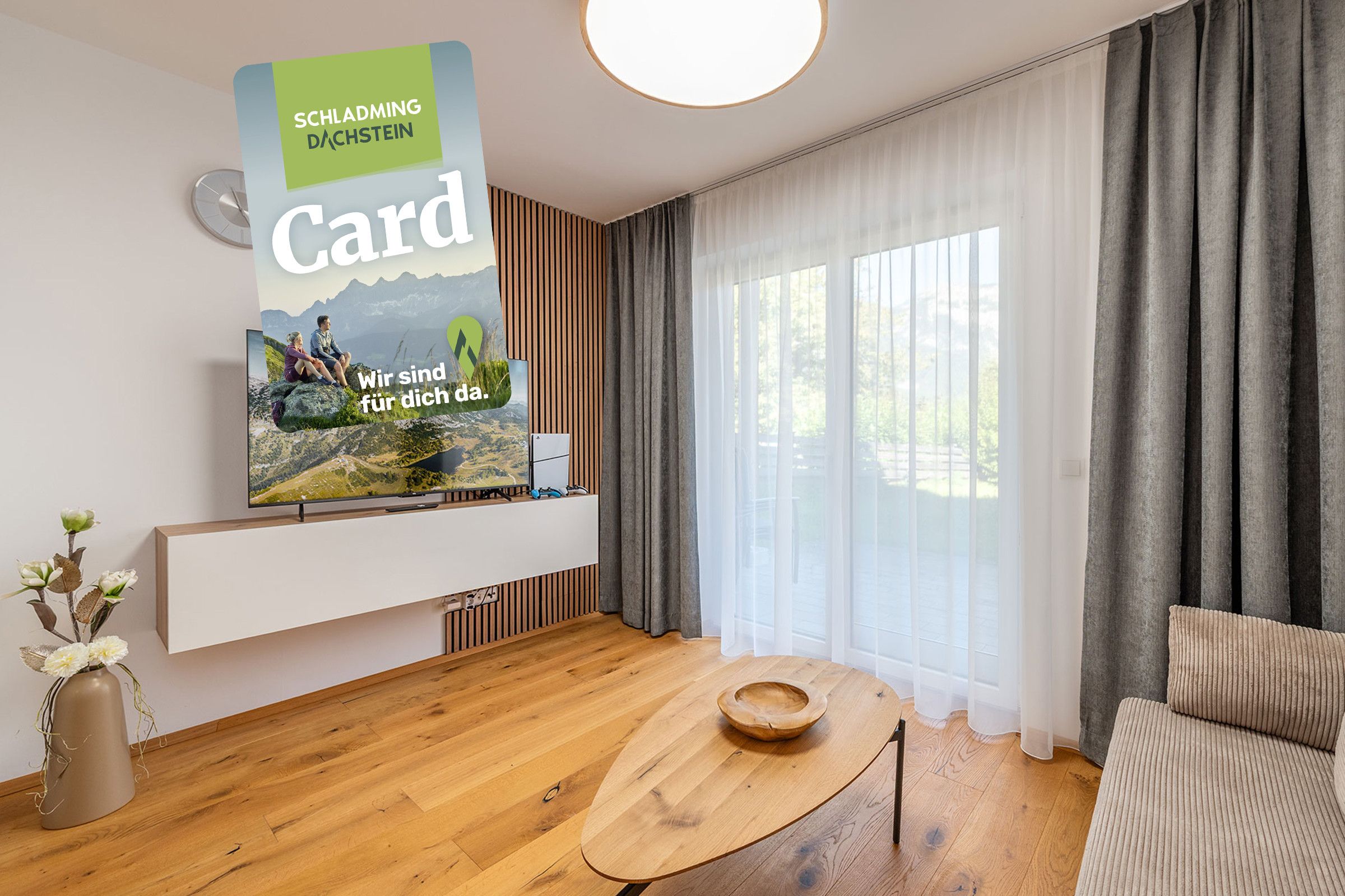 Ein modernes Wohnzimmer mit einem wandmontierten Fernseher, der eine schöne Landschaft zeigt, einem Holztisch, einer Couch und einem Fenster mit durchsichtigen Vorhängen.