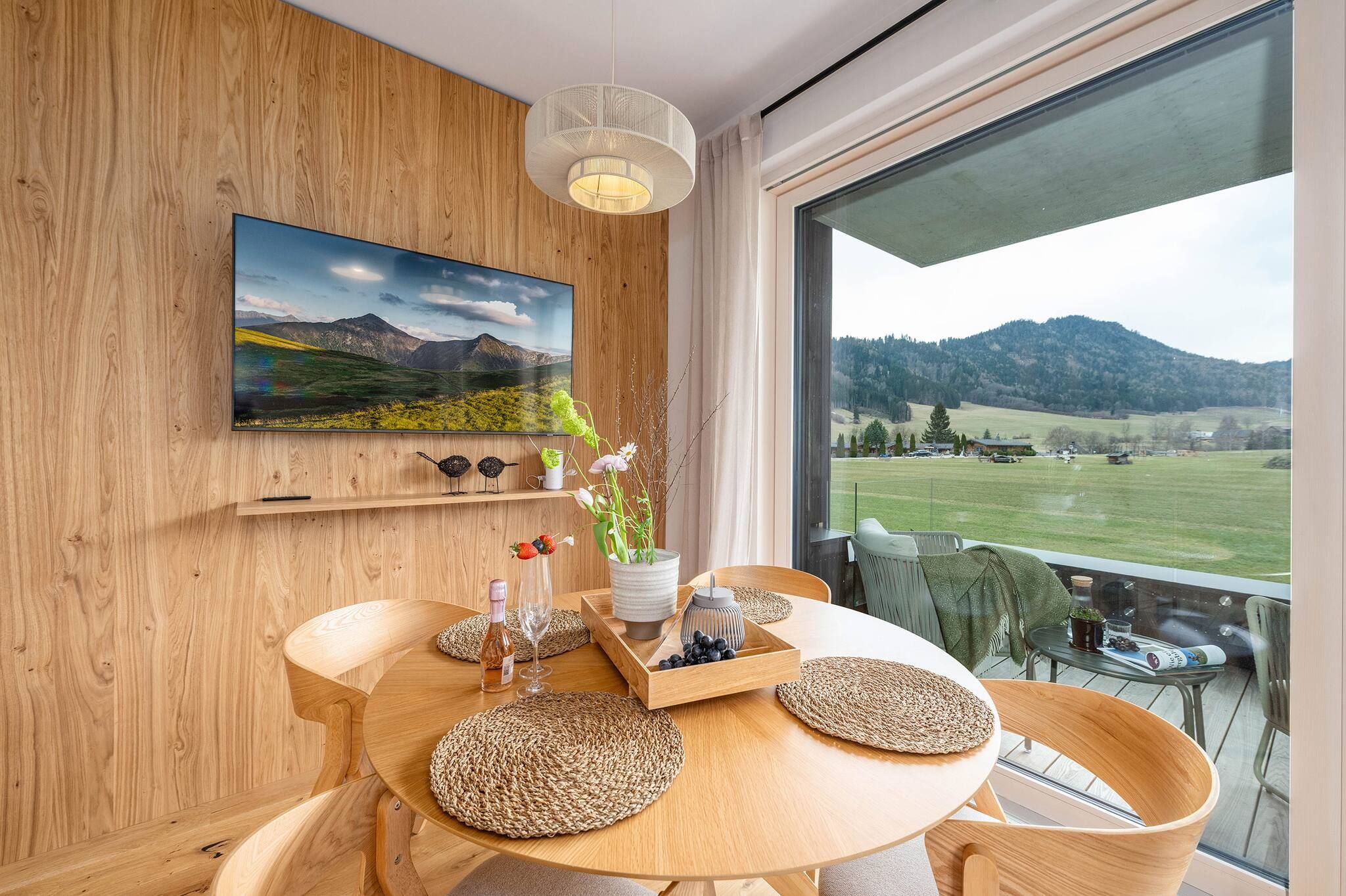 Ein Essbereich mit Holztisch, gewebten Unterlagen, einer Blumenvase und einem Landschaftsbild.