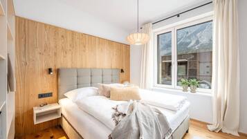 Ein modernes Schlafzimmer mit einem hölzernen Kopfteil, einem großen Bett mit weißer Bettwäsche, einem Nachttisch mit Lampe und einem Fenster mit Vorhängen.