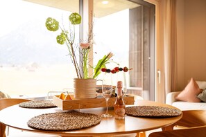 Une table ronde en bois, surmontée d’un set de table en fibres tressées, un vase contenant des fleurs vertes en forme de sphères, une bouteille en verre et un livre intitulé « Mon nid ».