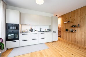 Une cuisine moderne avec des meubles blancs, un four encastré et un mur d’accent en bois.