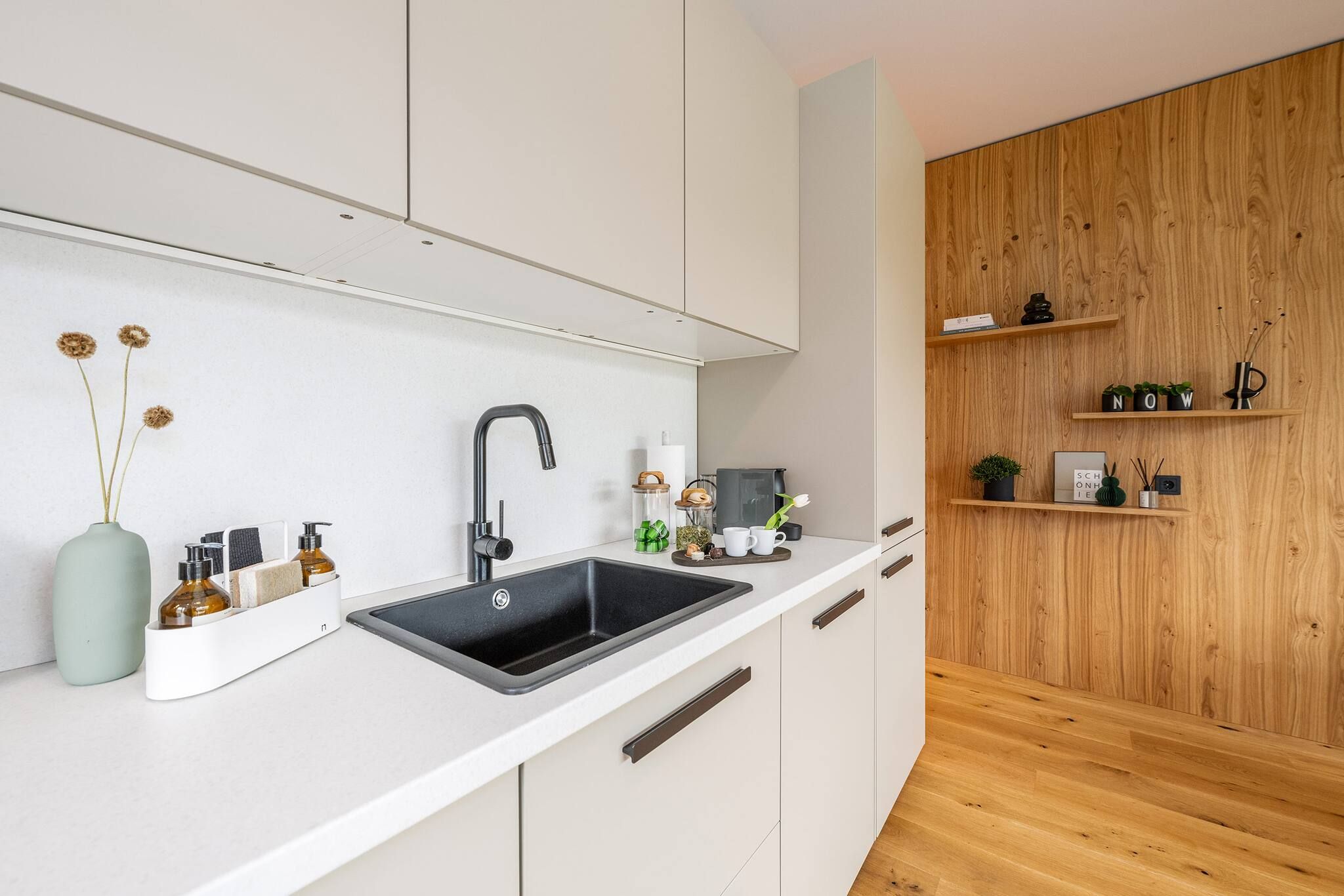 A modern kitchen with a black sink, white cabinets, and wooden shelves.