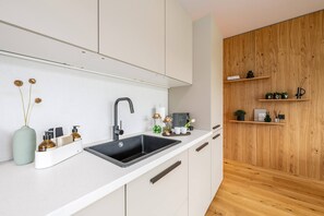 A modern kitchen with a black sink, white cabinets, and wooden shelves. - Mountain Paradise - Grimming 4 (Gröbming)