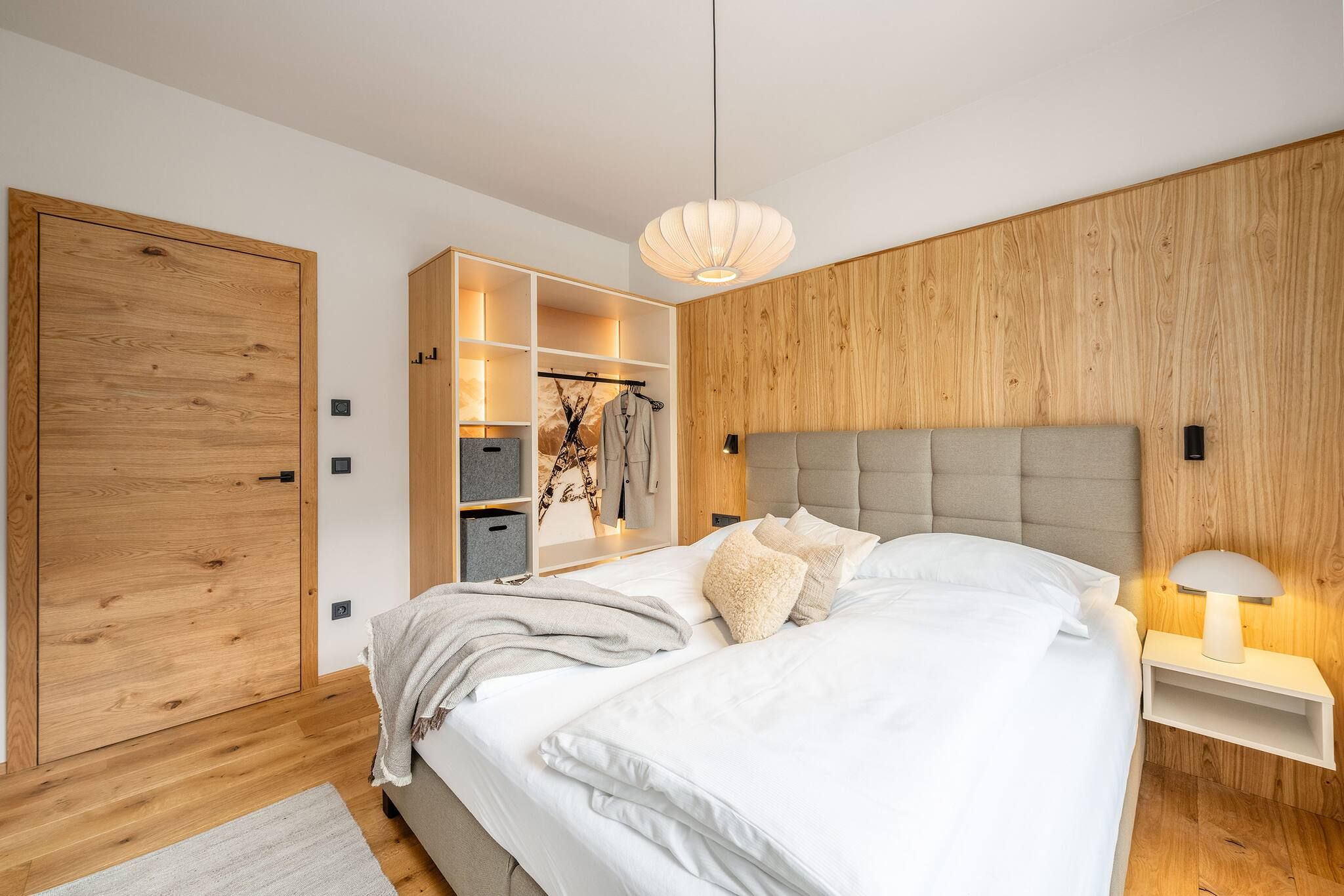 Una camera da letto moderna con un letto grande, un'armadio in legno, scaffalature integrate e una lampada a sospensione.