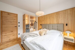 A modern bedroom with a large bed, wooden wardrobe, built-in shelving, and a pendant light. - Mountain Paradise - Grimming 4 (Gröbming)