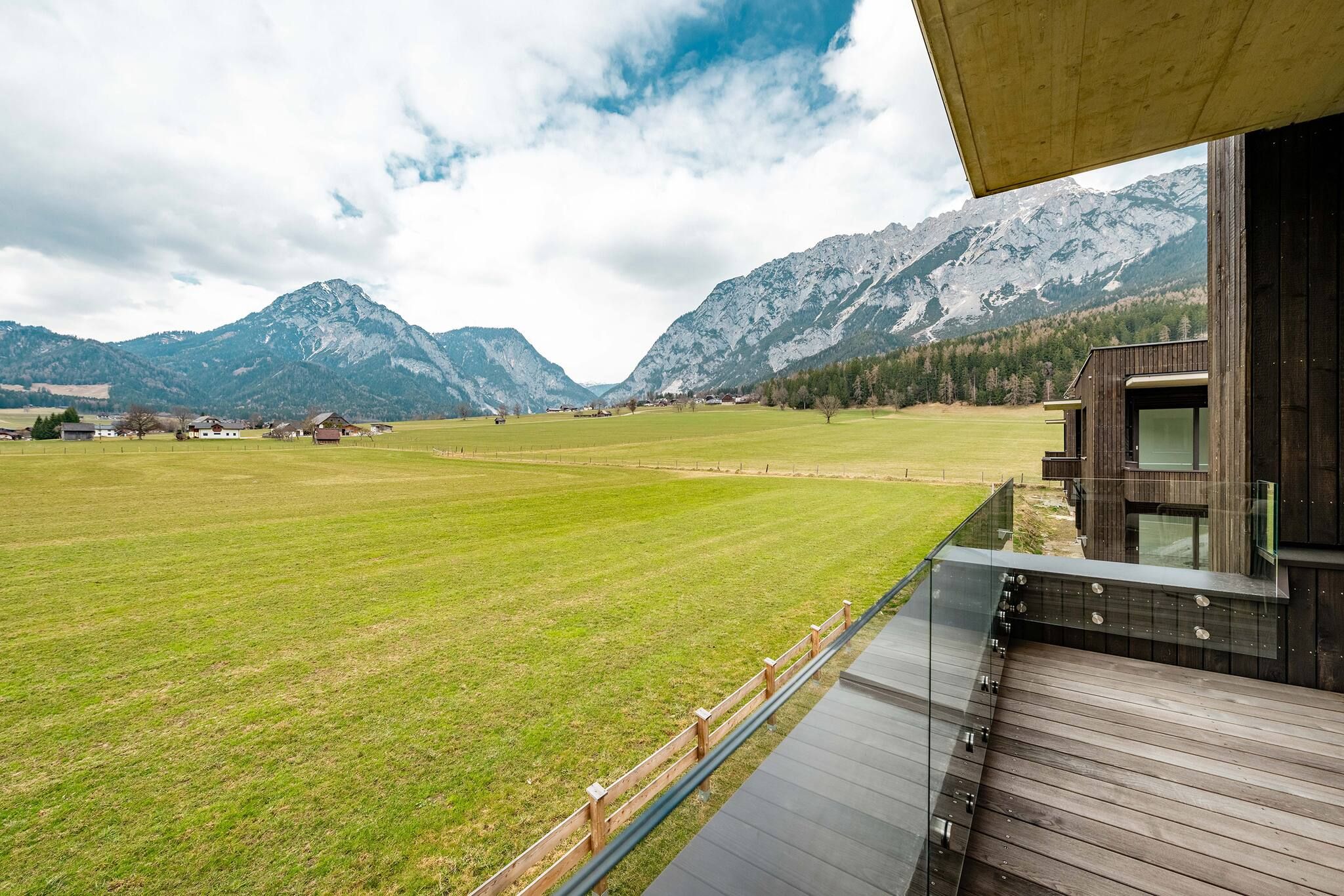 Ein modernes Gebäude mit einer Terrasse mit Blick auf ein grünes Feld und Berge.