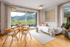 A modern living room with a large window, a sofa, a dining table with chairs, and a view of mountains. - Mountain Paradise - Grimming 4 (Gröbming)