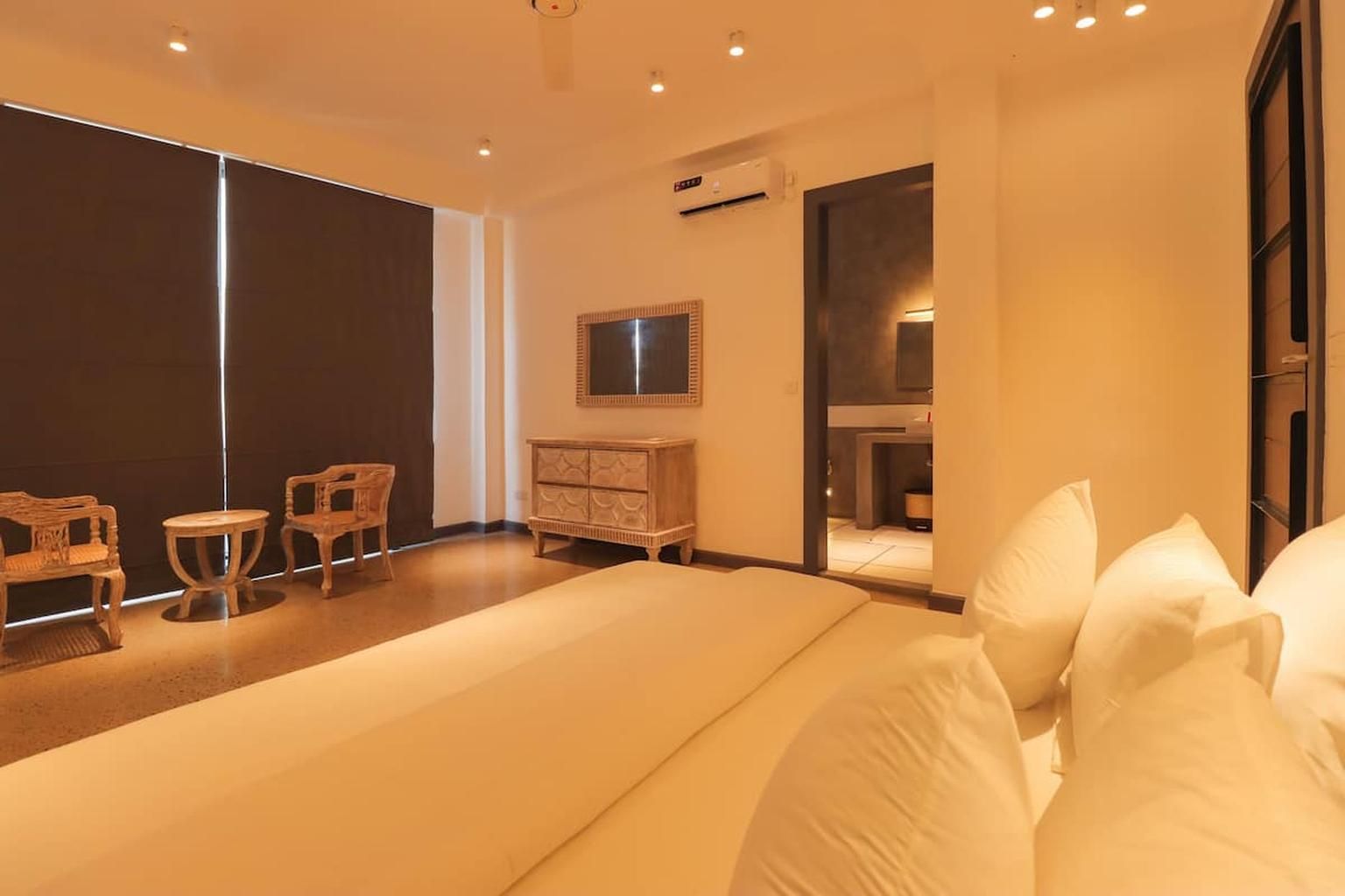 Une chambre d’hôtel avec un grand lit, une commode en bois, une télévision et un coin salon avec des fauteuils.