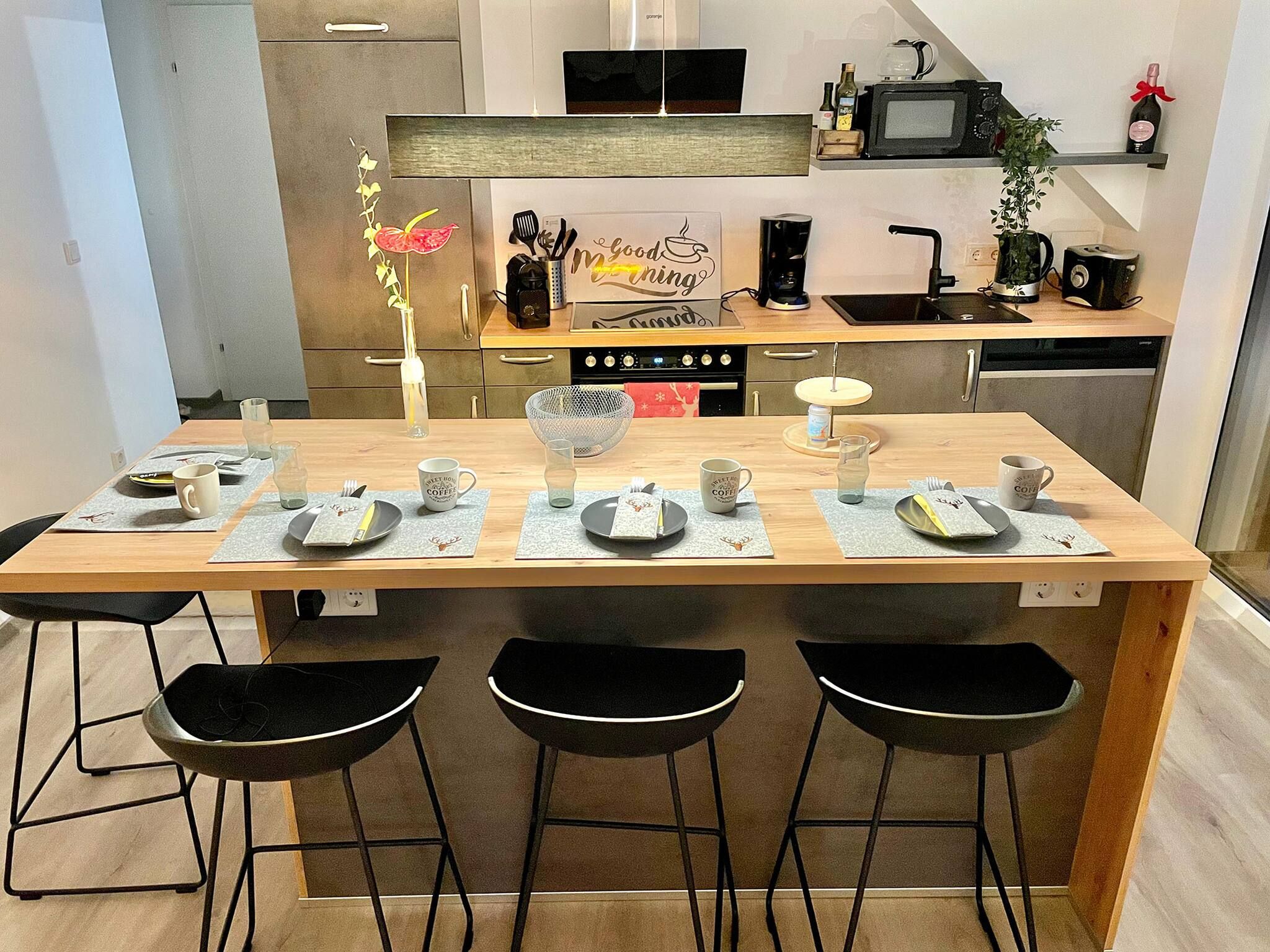 A modern kitchen with a central island, bar stools, and a coffee station.