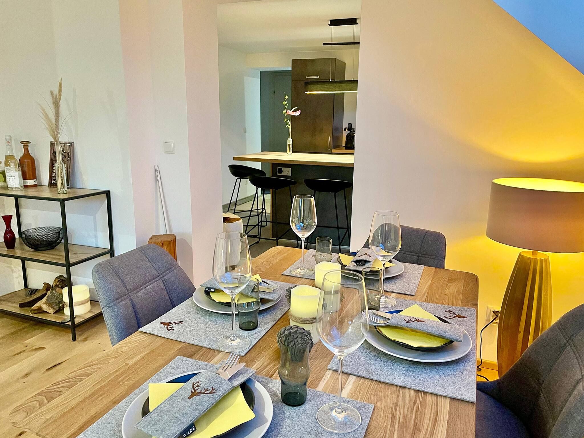 Een eetgedeelte met een houten tafel gedekt voor vier personen, inclusief borden, bestek en glazen.