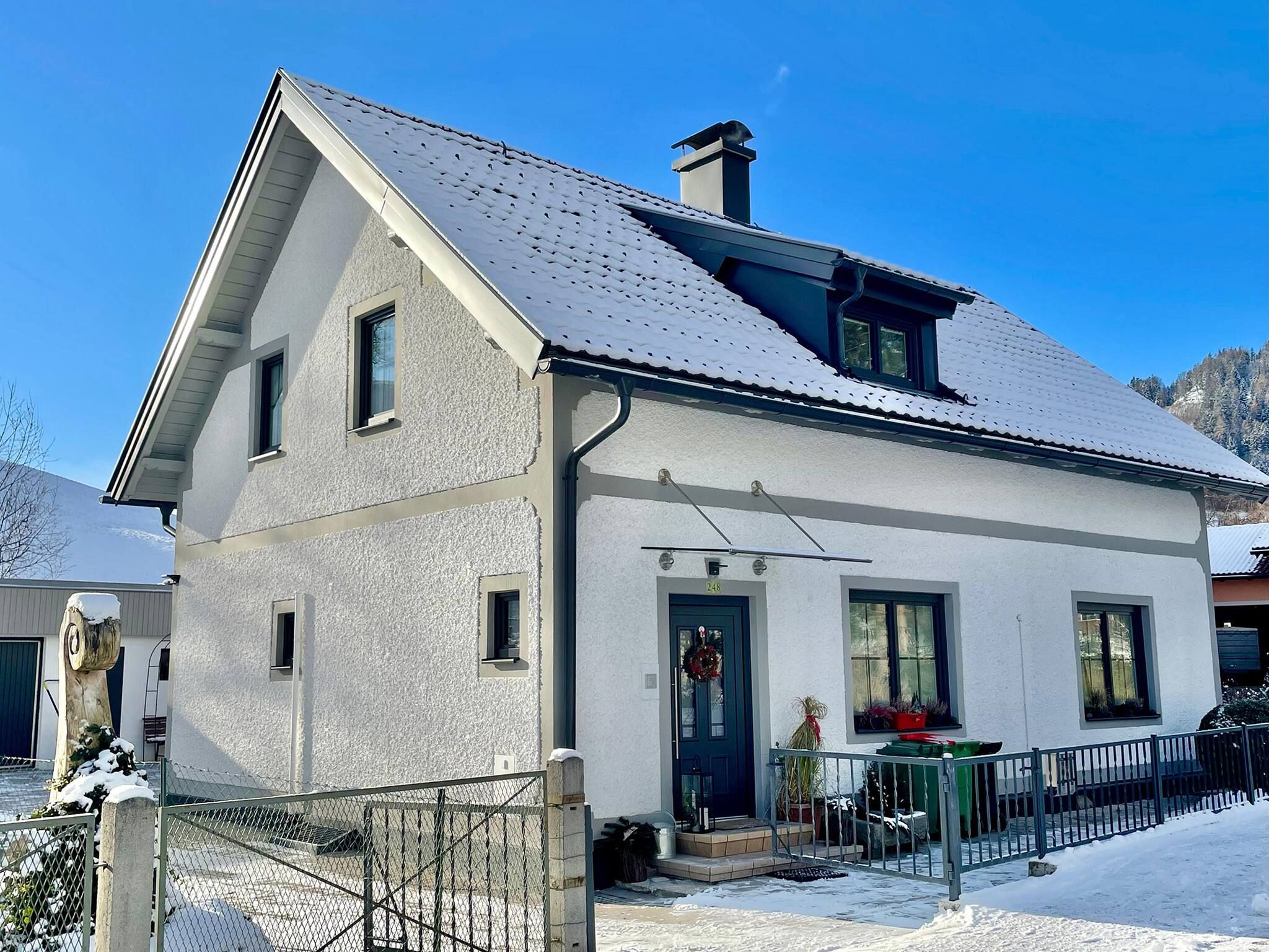 Una casa a due piani con tetto imbiancato dalla neve, un ingresso con ghirlanda e un cortile recintato.