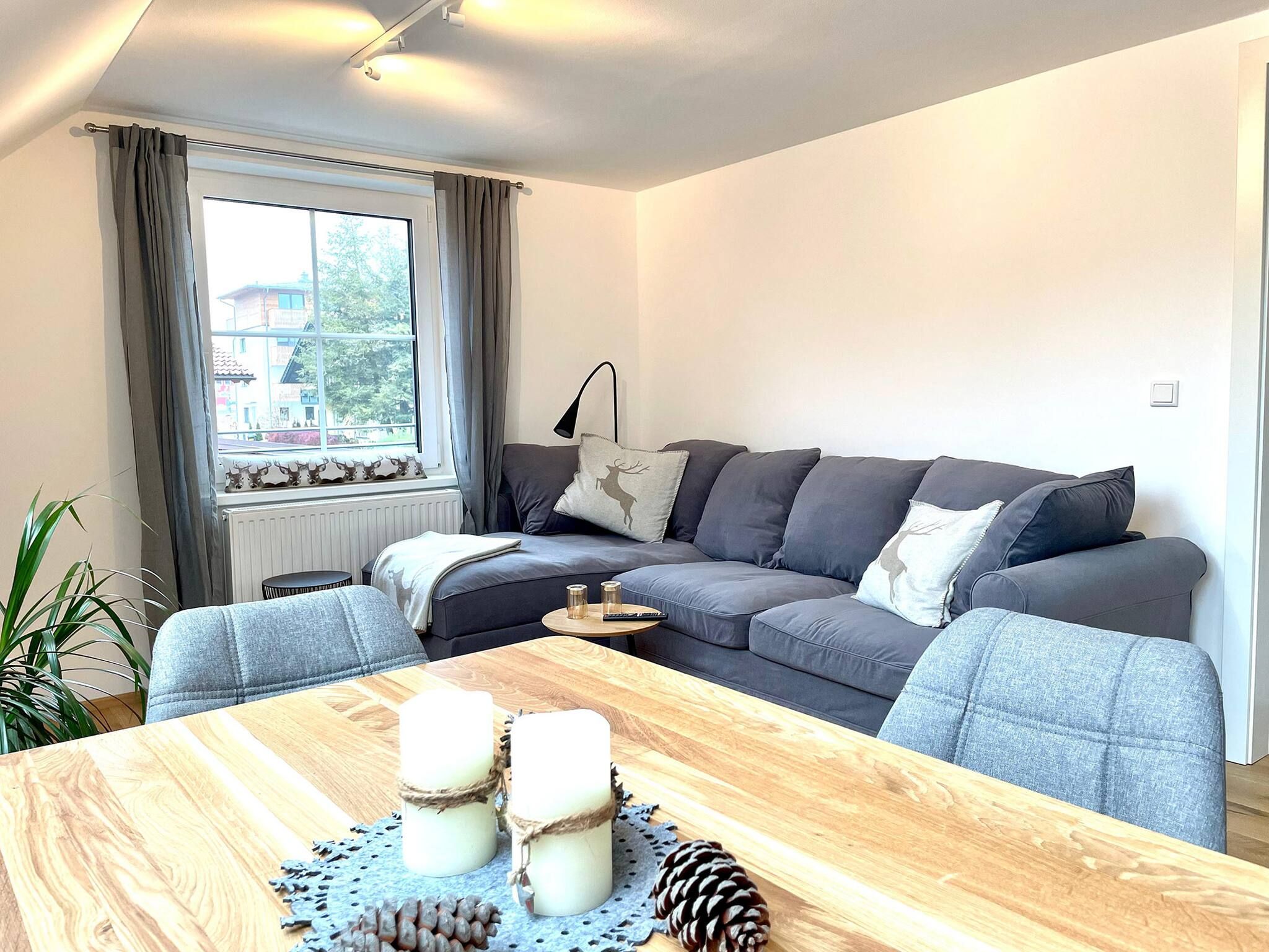 Een moderne woonkamer met een grijze bank, een houten salontafel en een raam met gordijnen.