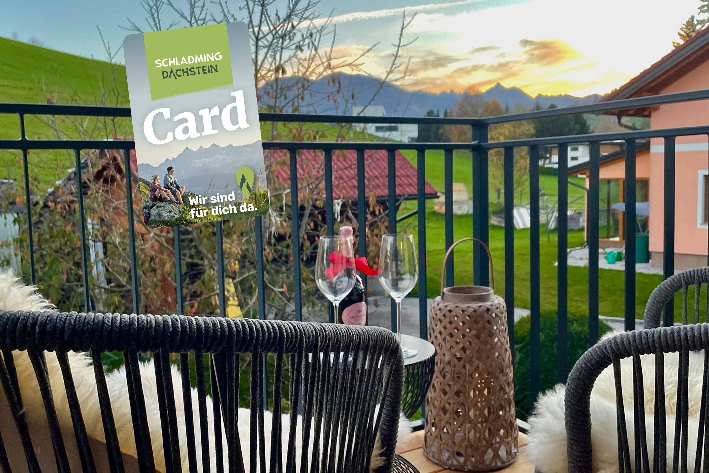 Un balcone con vista su un paesaggio montuoso, un tavolo con una bottiglia di vino e un cartello con del testo.
