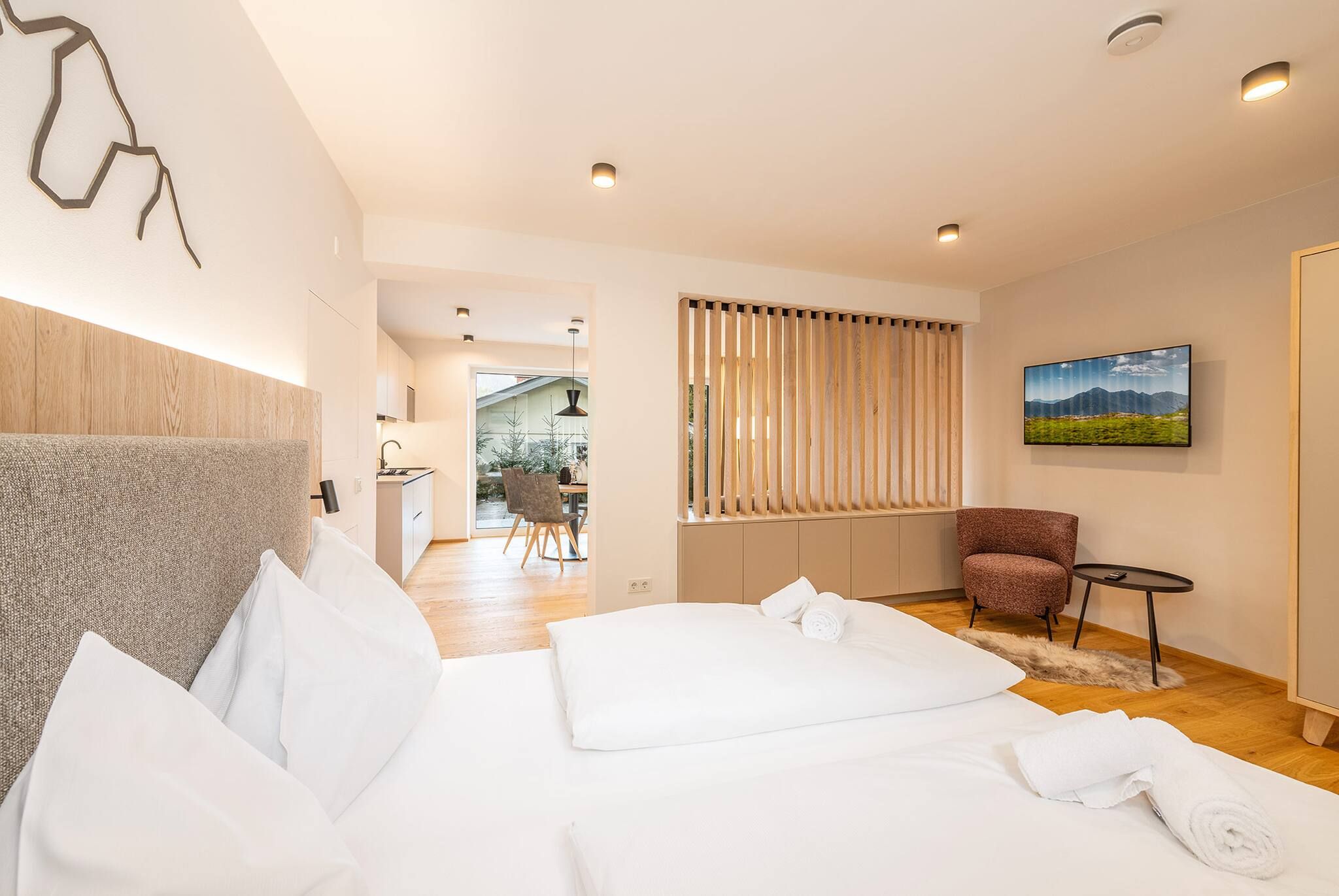 Habitación de hotel moderna con una cama grande, zona de estar con una silla y una mesita, y vistas al exterior.