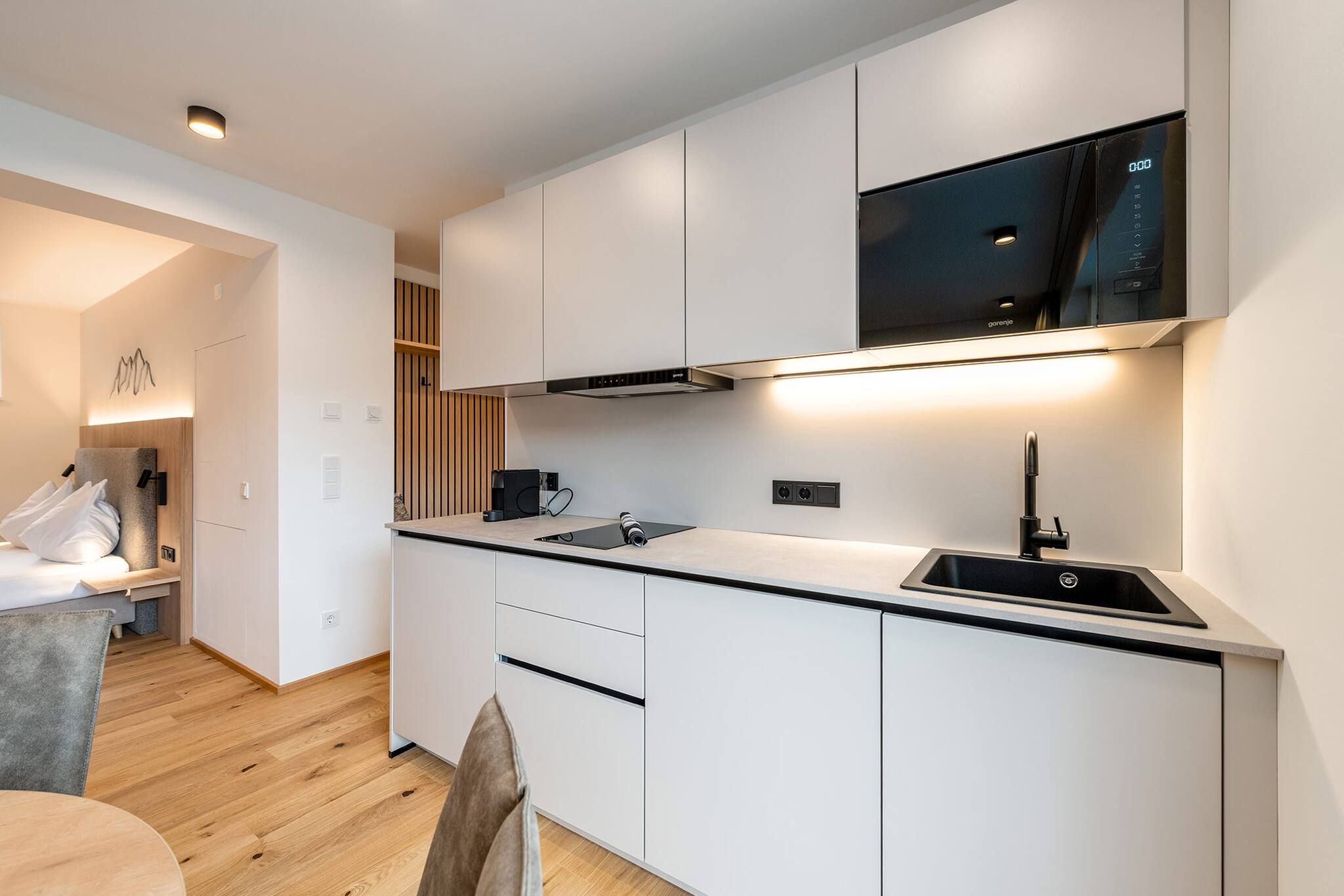 A modern kitchen with white cabinetry, a black countertop, and a built-in oven.