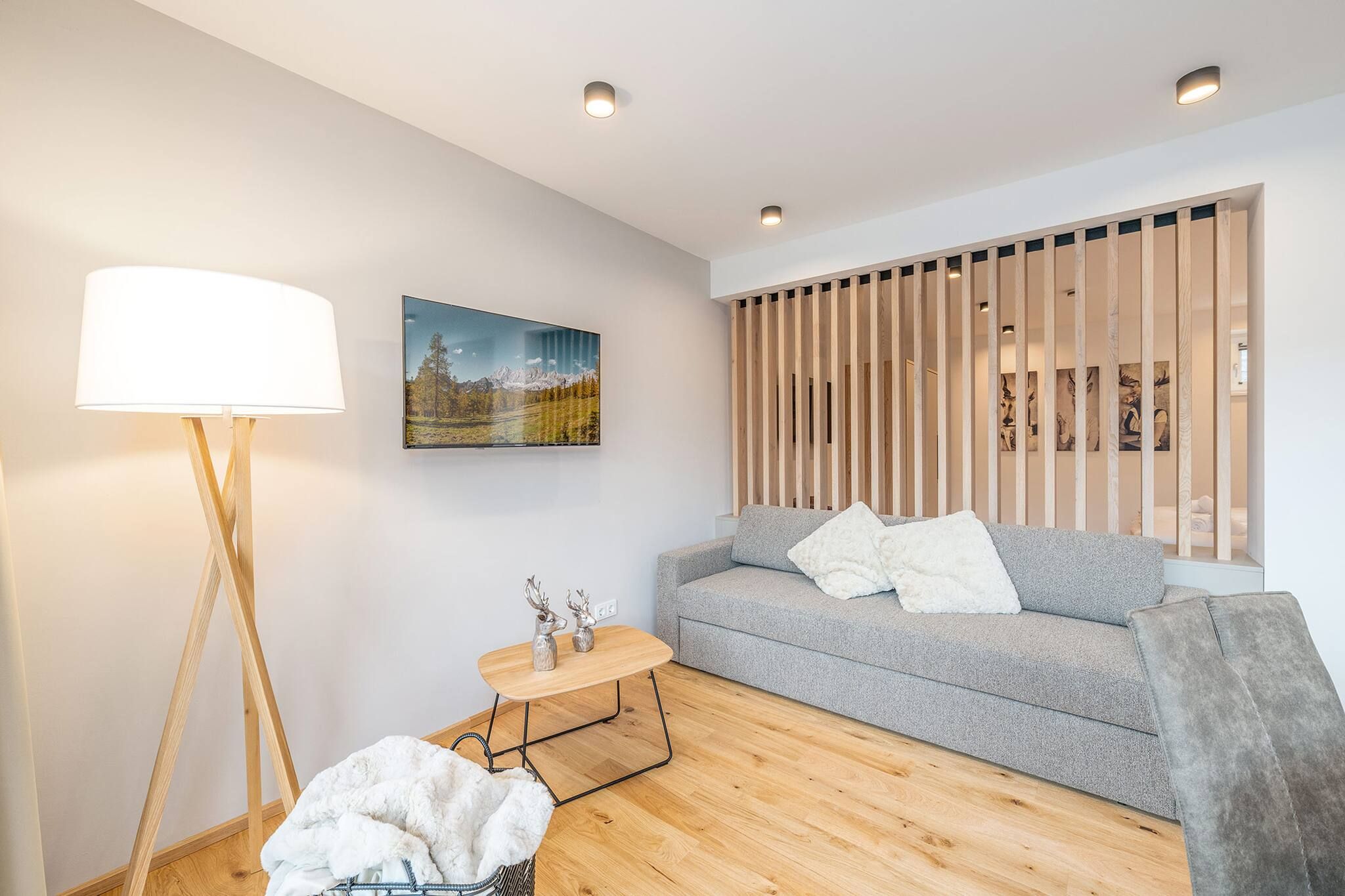 Una sala de estar moderna con un sofá gris, una mesa de centro redonda de madera, una lámpara de pie y un cuadro en la pared.