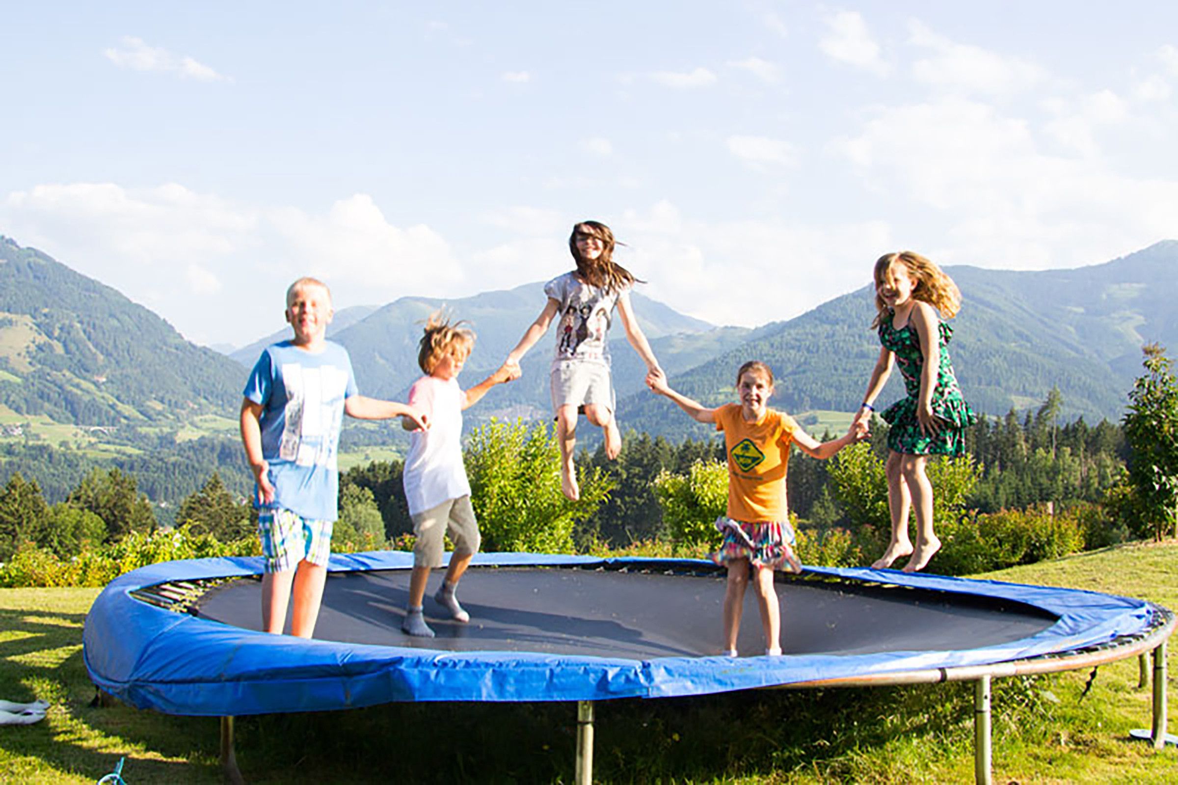 Un groupe de personnes sautant sur un trampoline, avec un paysage montagneux en arrière-plan.