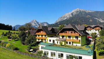 Ein traditionelles Chalet-Hotel mit mehreren Balkonen, vor einer Bergkulisse und blauem Himmel.