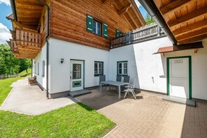 Ein Holzhaus mit Balkon und überdachter Terrasse, wobei eine Tür mit der Aufschrift 'Ski- und Müllraum' versehen ist.