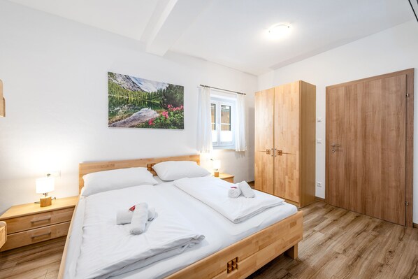 Un dormitorio con una cama de madera, dos mesitas de noche, una ventana con cortinas, un armario de madera y un cuadro en la pared.