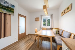 Ein Zimmer mit einem Holztisch, einer Bank, einem Fenster mit Blick auf Grünflächen und einer Holzverkleidung an der Wand.