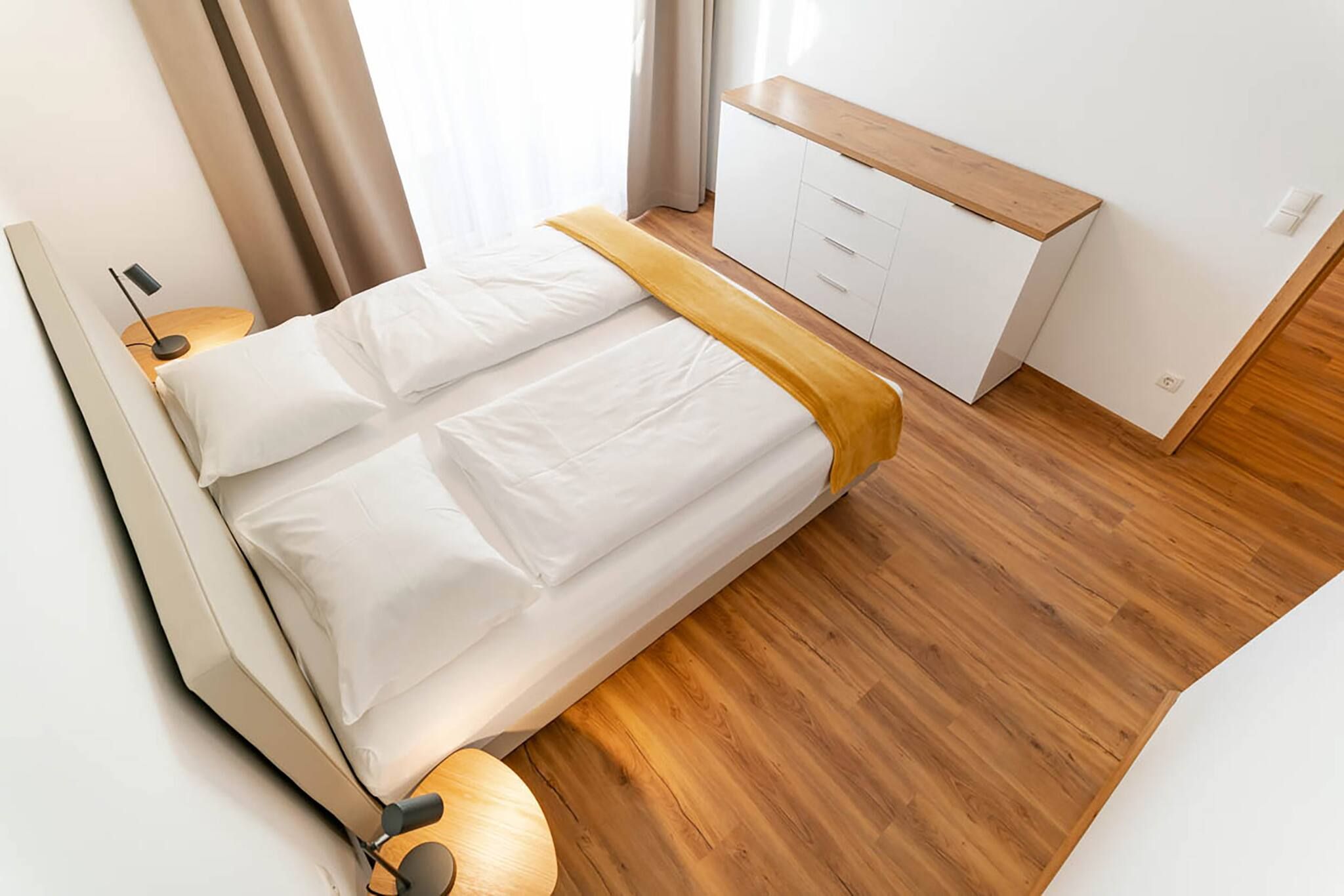 Ein modernes Schlafzimmer mit einem Bett, Nachttischlampen, Holzboden und einer weißen Kommode.