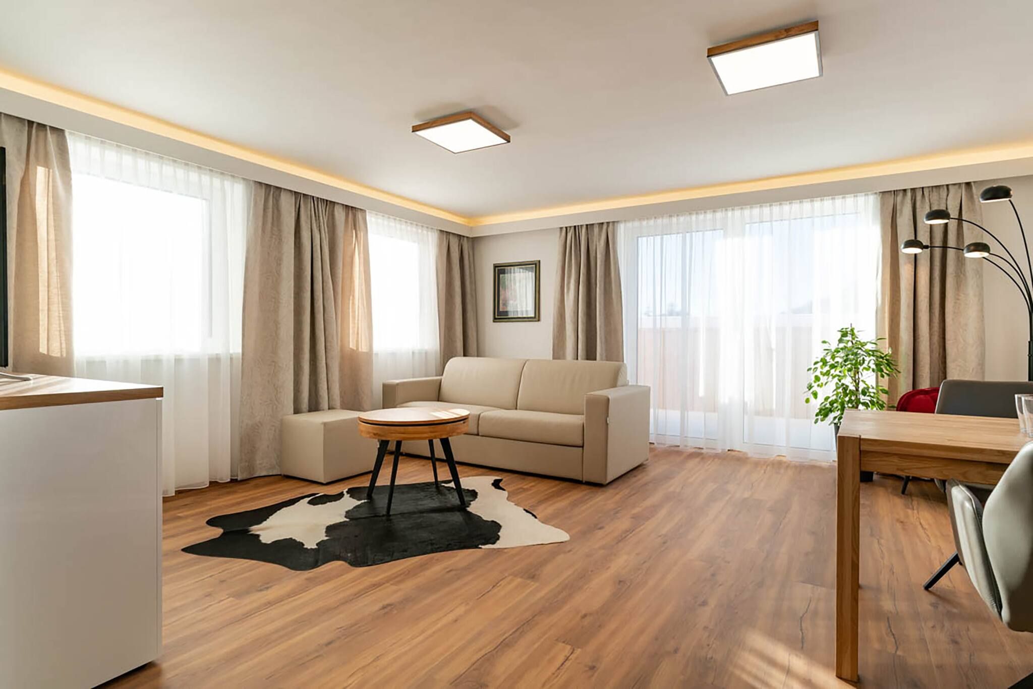 A modern living room with a sofa, a round coffee table, a desk with a chair, and a potted plant.