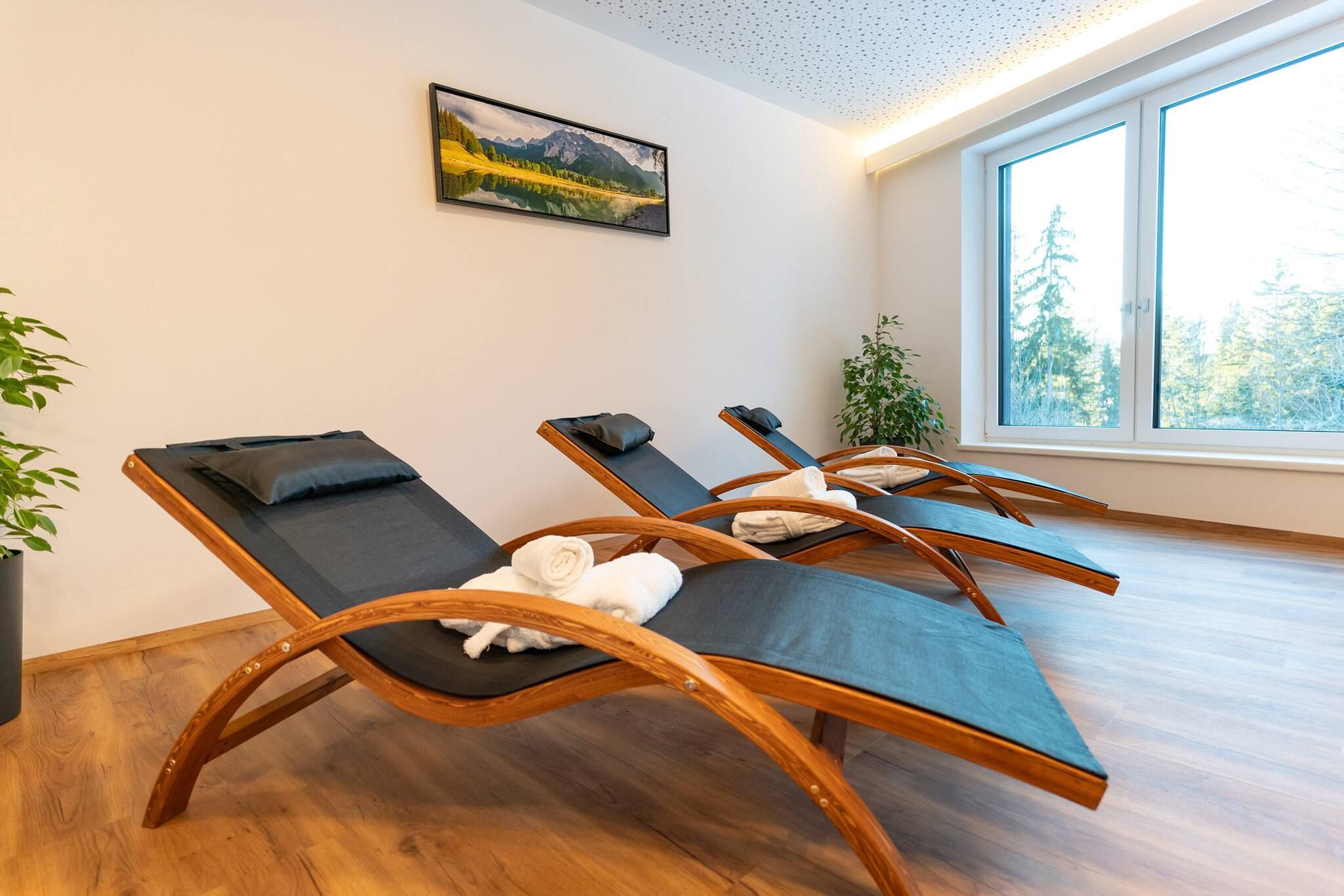 Ein Zimmer mit drei gepolsterten Loungesesseln mit Holzrahmen, einem großen Fenster mit Blick auf Bäume und einem Gemälde an der Wand.