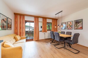 Ein modernes Wohnzimmer mit einer Couch, einem Esstisch mit Stühlen und einem Balkon mit Vorhängen.