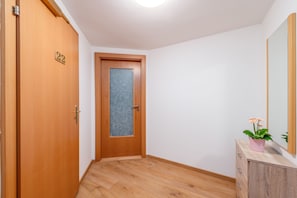Un pasillo con una puerta de madera numerada 22, un armario de madera con espejo y una planta en maceta.