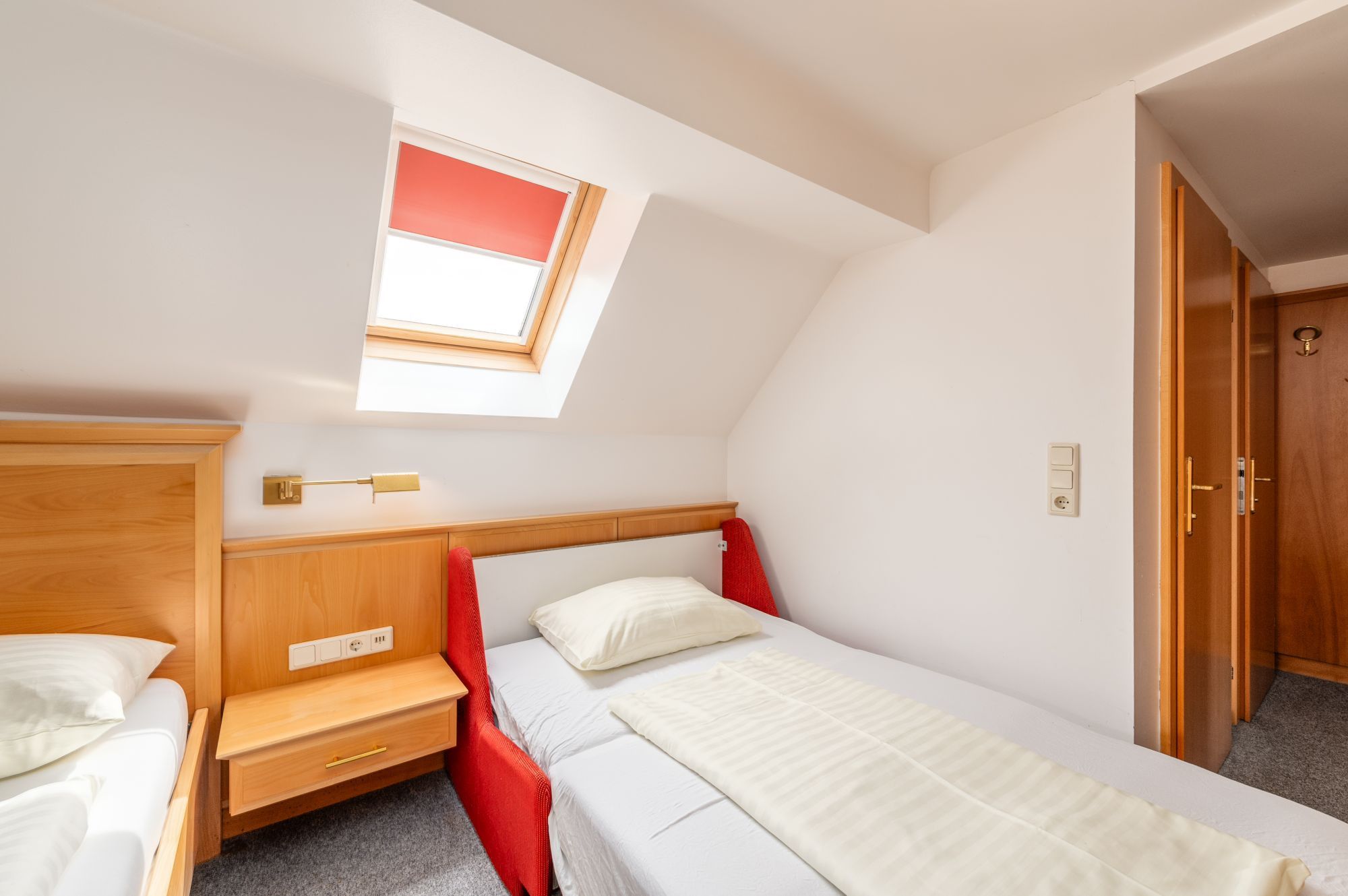 Ein Schlafzimmer mit einem Oberlicht, einem Holzschrank, einem Nachttisch und einer roten Akzentwand.