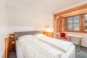 Ein Hotelzimmer mit Bett, Nachttisch, Lampe, Stuhl und einem Fenster mit Vorhängen.