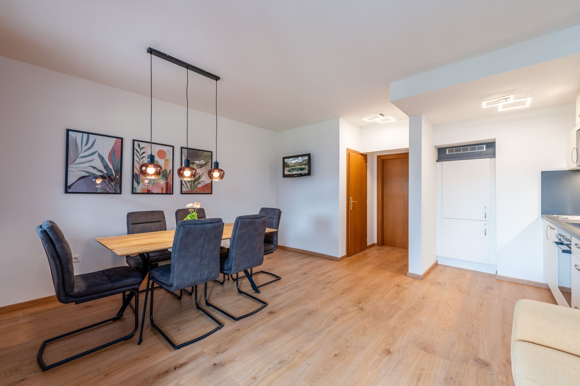 Een moderne eetruimte met een houten tafel, stoelen, hanglampen en kunstwerken in lijsten aan de muur.