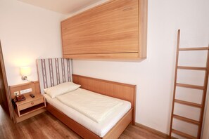 Un llit individual amb capçalera de fusta, una taula de nit amb una làmpada i un armari a la part superior.
