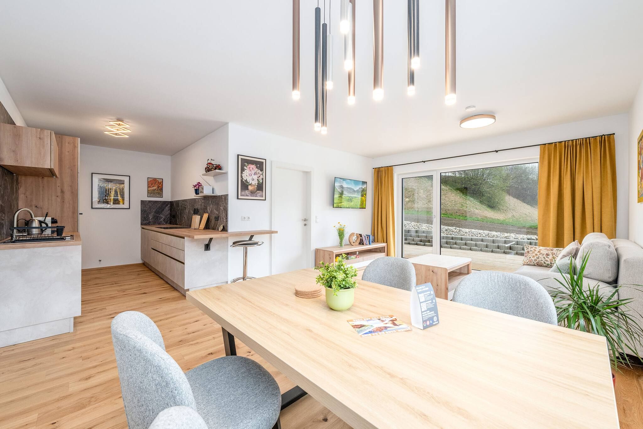 Una cocina moderna con encimera de madera, un comedor con mesa de madera y un sofá con vistas a un jardín.