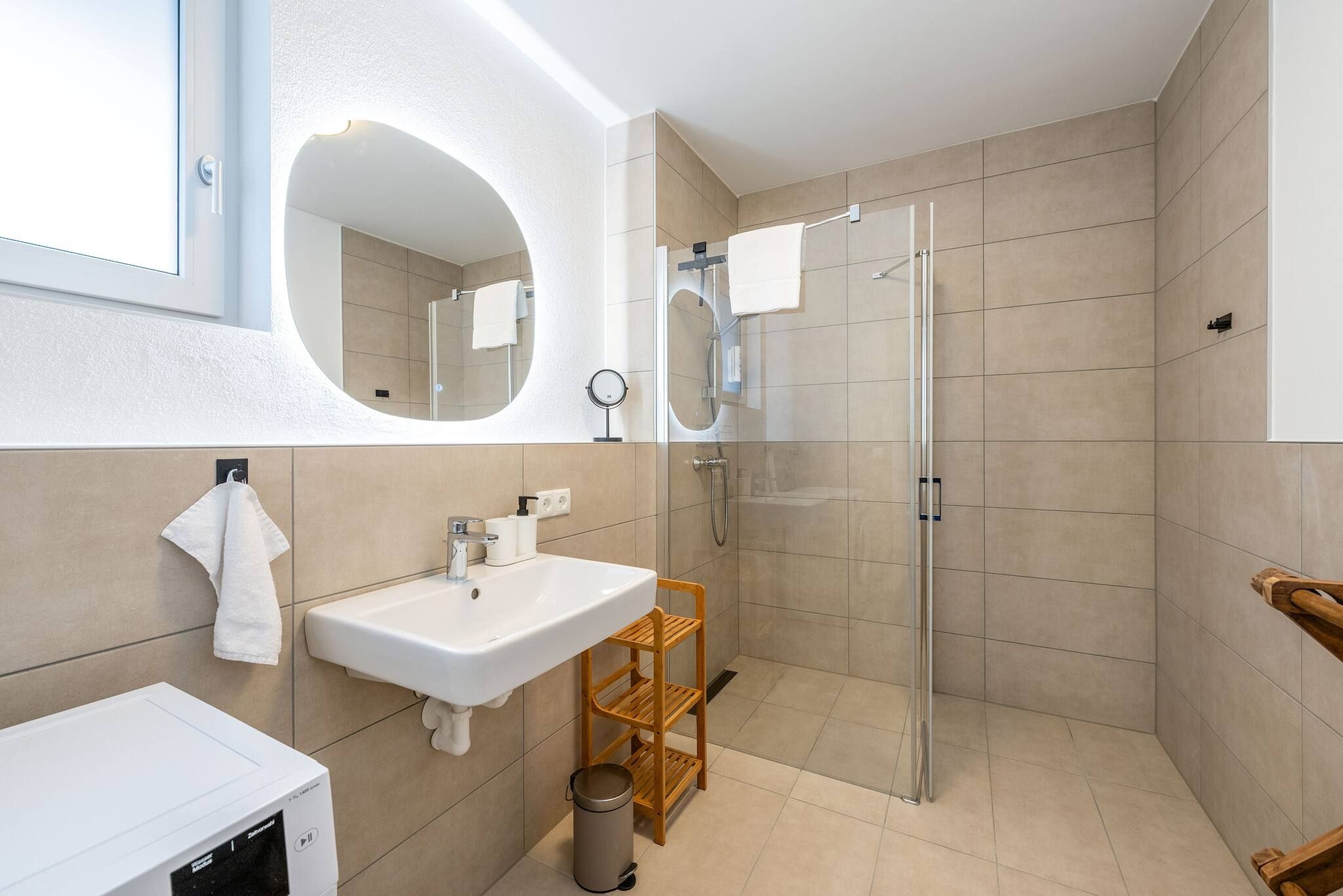 Ein modernes Badezimmer mit einer Duschkabine aus Glas, einem weißen Waschbecken und einem Holzregal.
