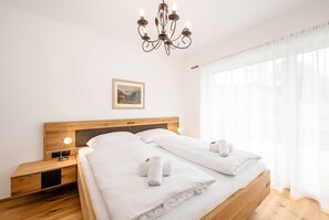 Ein Hotelzimmer mit einem hölzernen Bett, weißen Leinentüchern, einer Nachttischlampe, einem gerahmten Bild an der Wand und einer Chandelüstere.