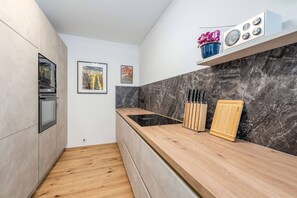 Eine moderne Küche mit einer Holzarbeitsplatte, einem Einbauofen, einer Marmor-Spritzschutzwand und einem kleinen Regal mit Dekoration.