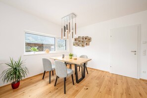 Ein Essbereich mit einem Holztisch, grauen Stühlen, einer Topfpflanze und einer Wandleuchte.
