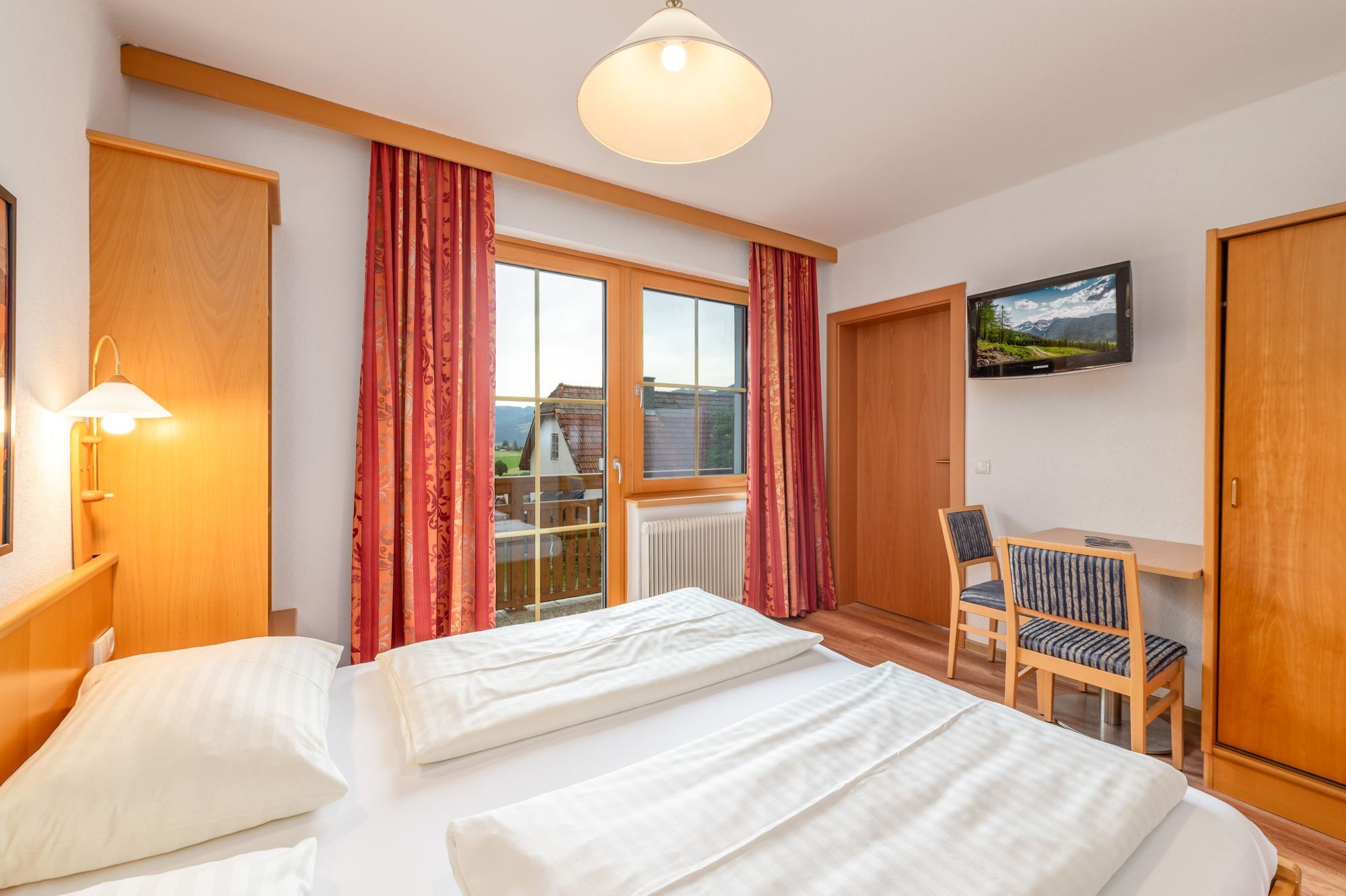 Una camera d'albergo con un letto, una scrivania, una sedia, una televisione e una finestra con tende.
