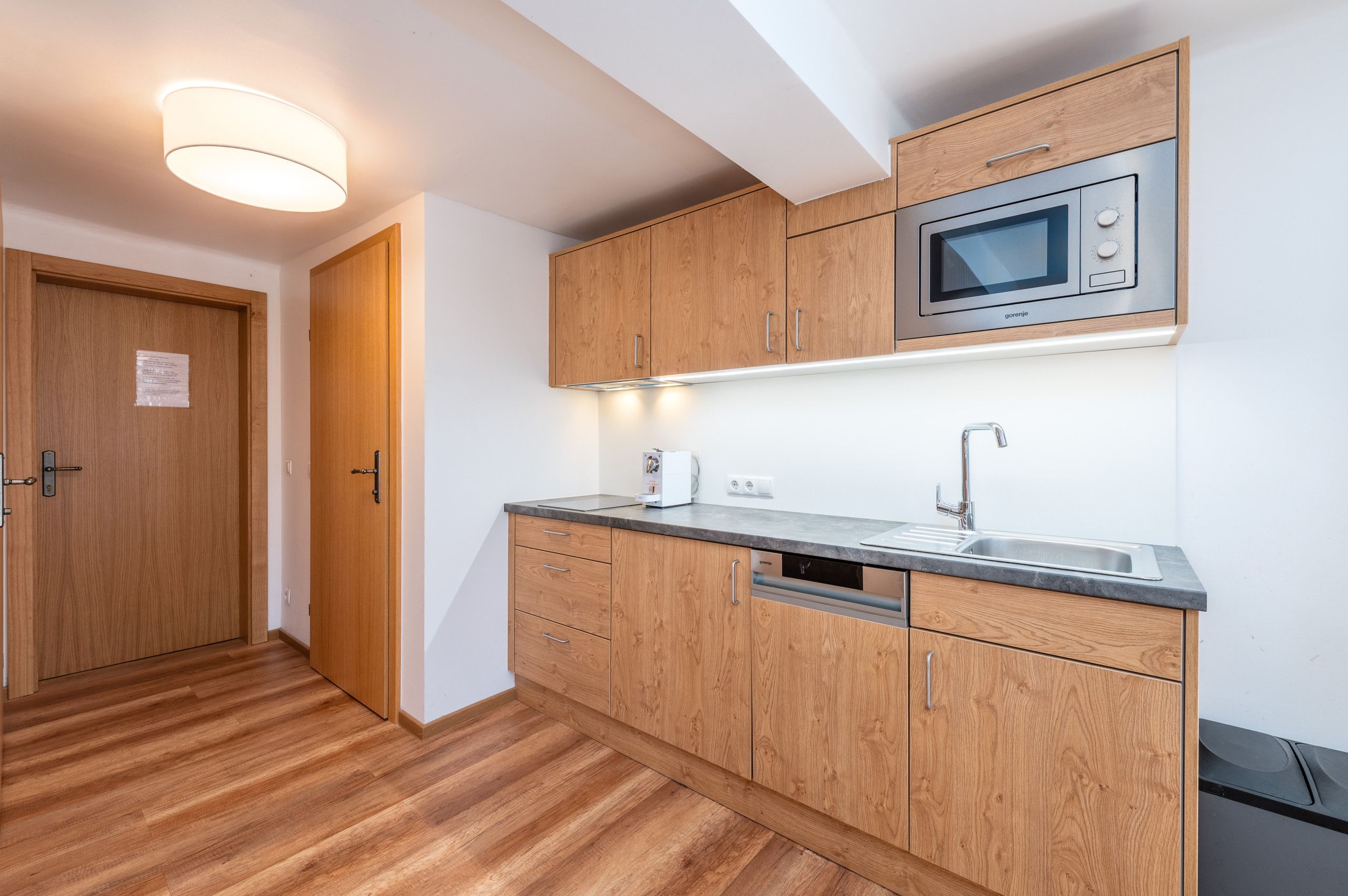 Una cucina compatta con mobili in legno, un forno a microonde integrato e un lavello in acciaio inossidabile.