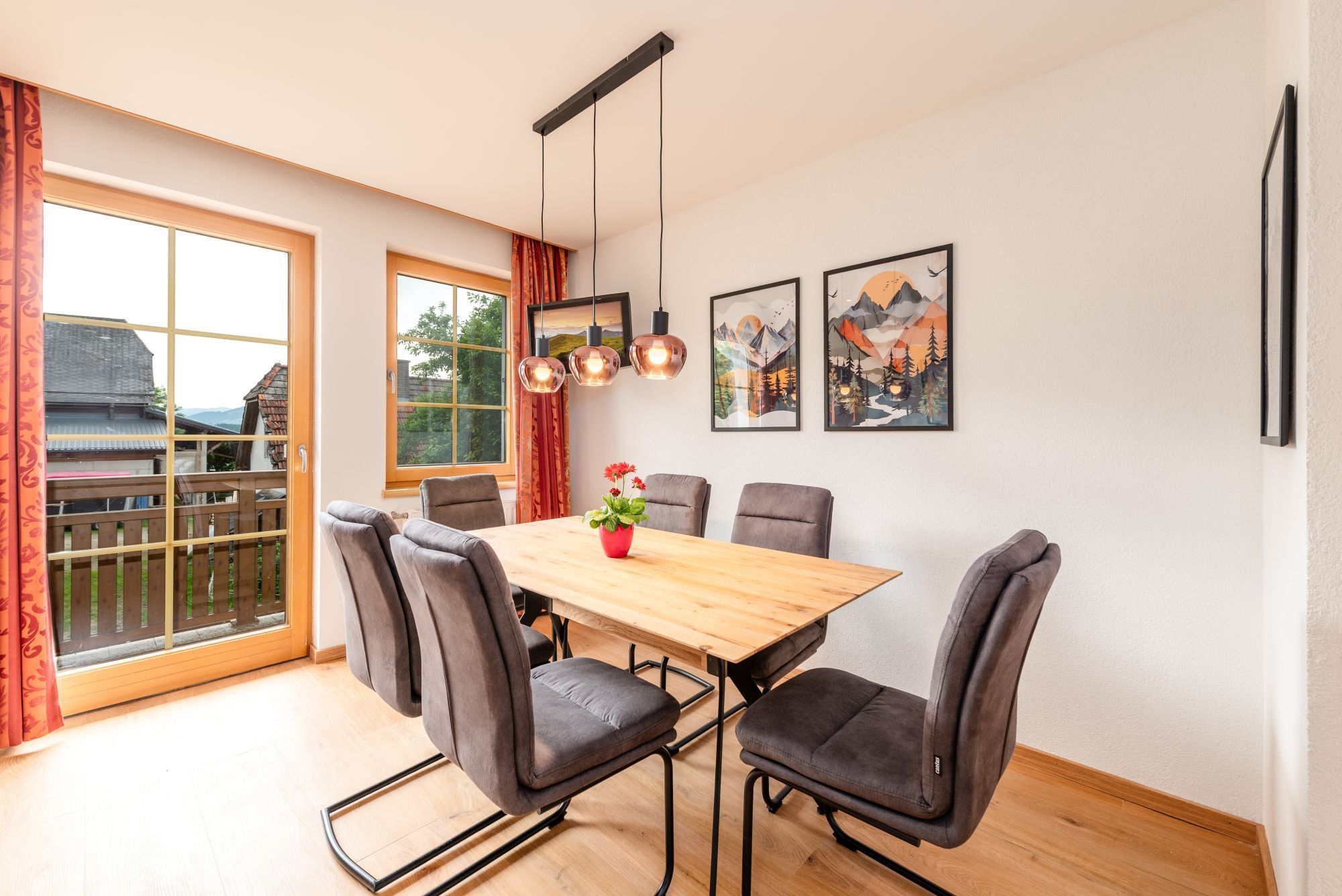 Un comedor con una mesa de madera y seis sillas, una planta en maceta y dos cuadros en la pared.