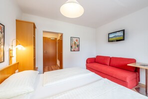 Una habitación de hotel con una cama, un sofá rojo, un televisor y una puerta que da a otra habitación.