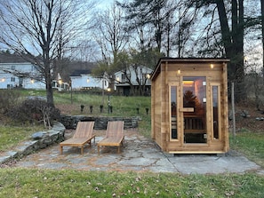 Une cabane en bois avec une porte en verre, deux fauteuils en bois et un mur de pierres, le tout situé dans un jardin.