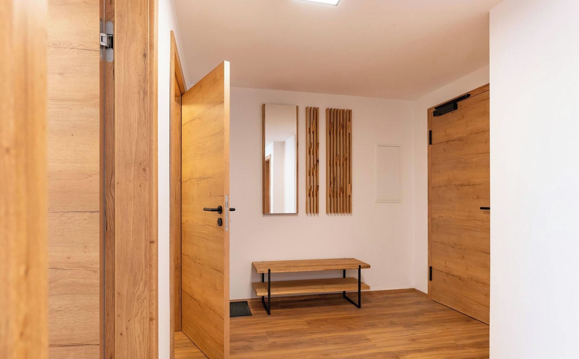 A hallway with wooden doors, a bench, and a mirror on the wall.