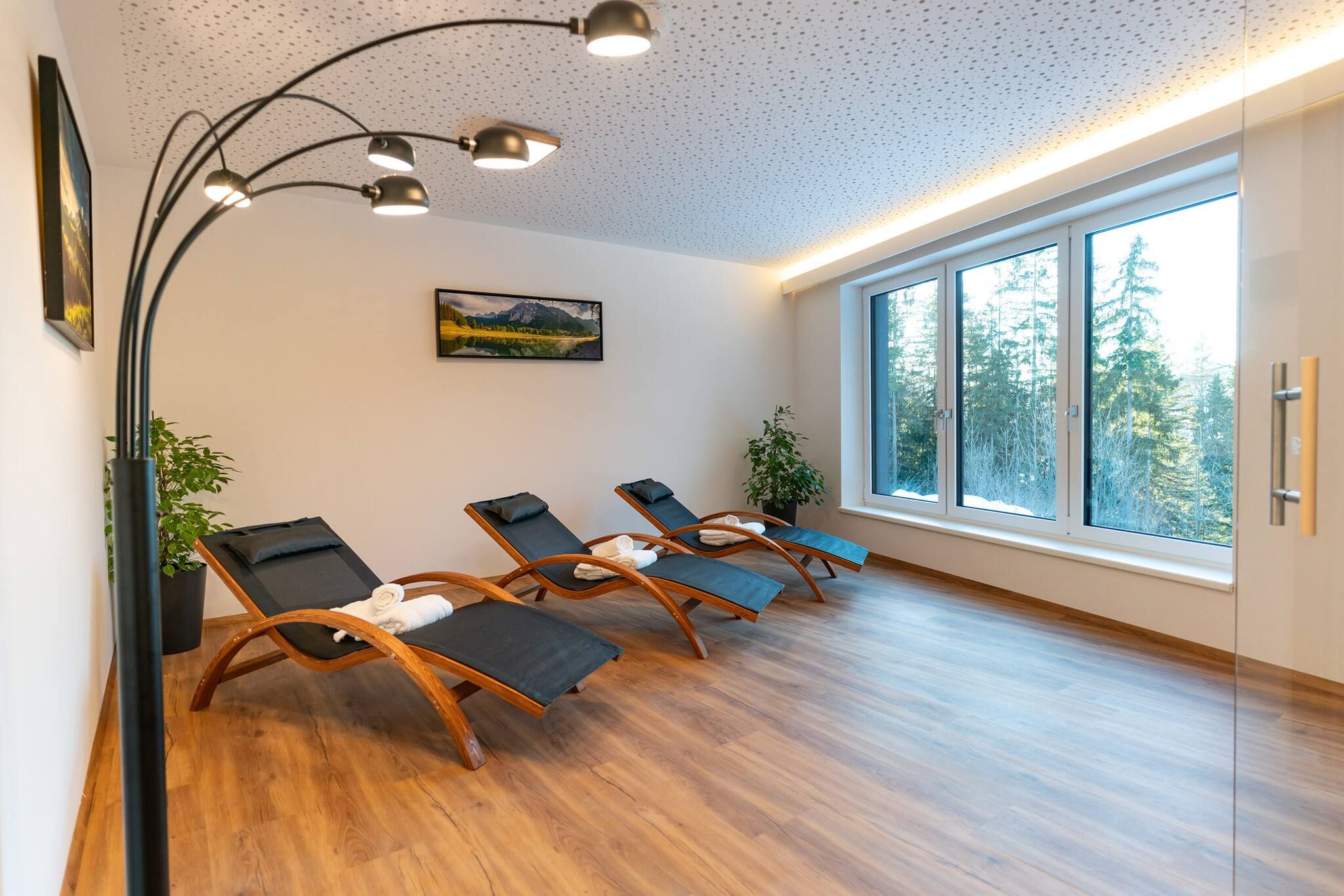 Ein Zimmer mit Holzboden, drei Sesseln, einem großen Fenster mit Blick auf Bäume und einer Decke mit einem einzigartigen Muster.