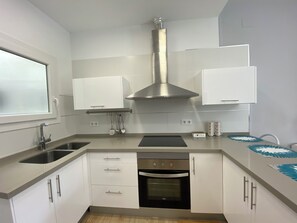 Cuina moderna amb armaris blancs, una campana extractora d'acer inoxidable, forn encastrat i una finestra.