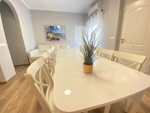 Zona de menjador amb taula blanca, cadires i una planta en test.