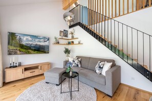 Ein modernes Wohnzimmer mit einem grauen Sofa, einem Couchtisch, einem Holzkabinett, einer Treppe mit schwarzer Geländer und einem großen Landschaftsbild an der Wand.