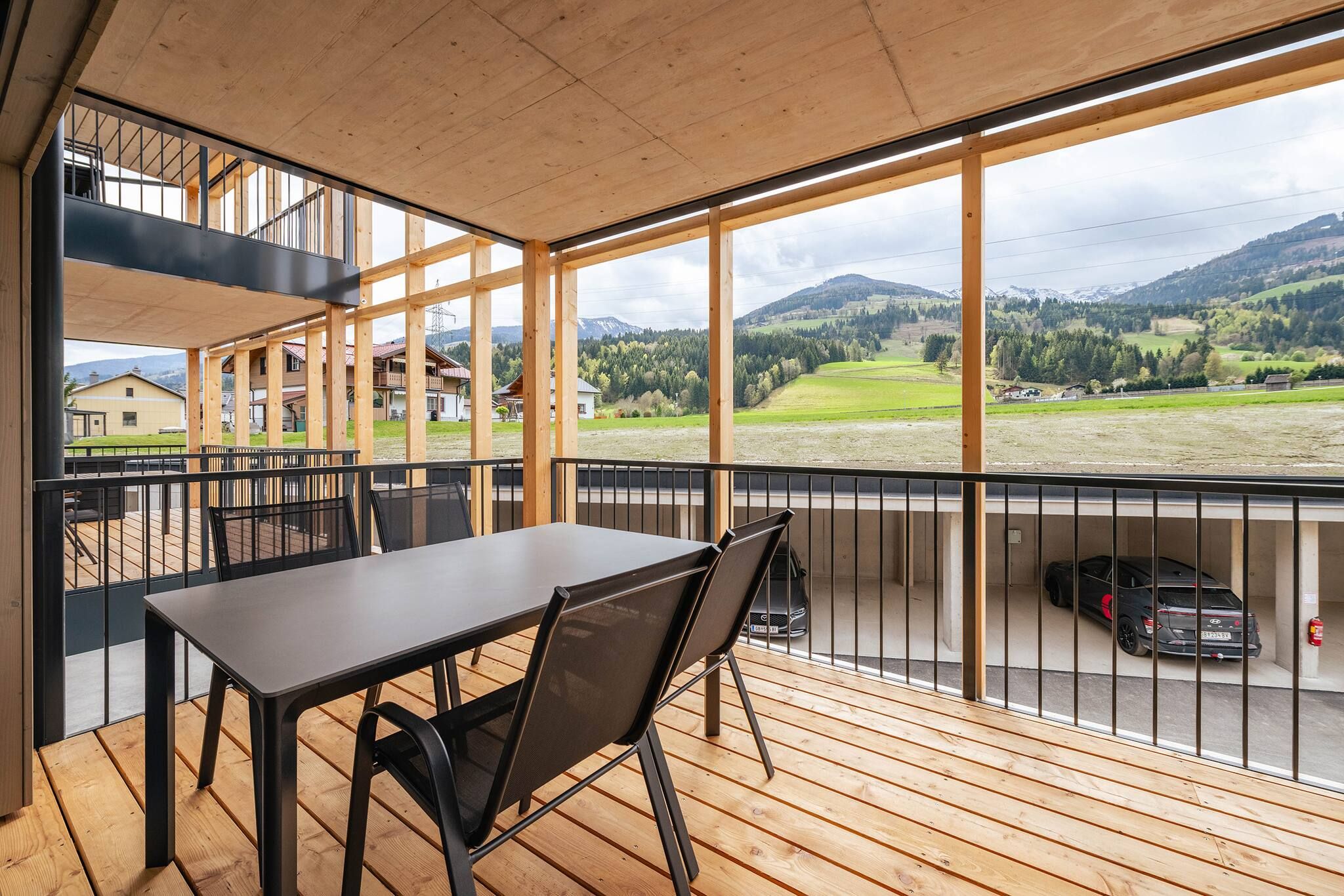Ein Balkon mit Tisch und Stühlen, der auf einen Parkplatz und eine reizvolle Landschaft blickt.
